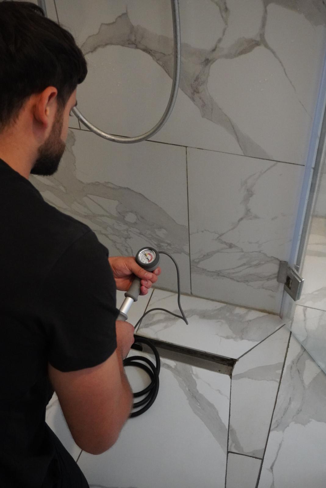 Julian Förster prüft mit einem Manometer die Abdichtung einer bodengleichen Dusche.